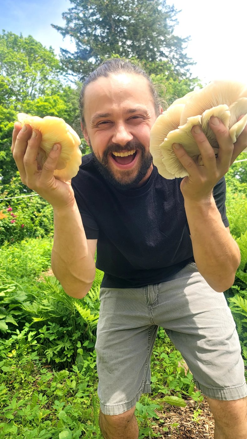 Matthew Getzin holding two large mushrooms in the forest